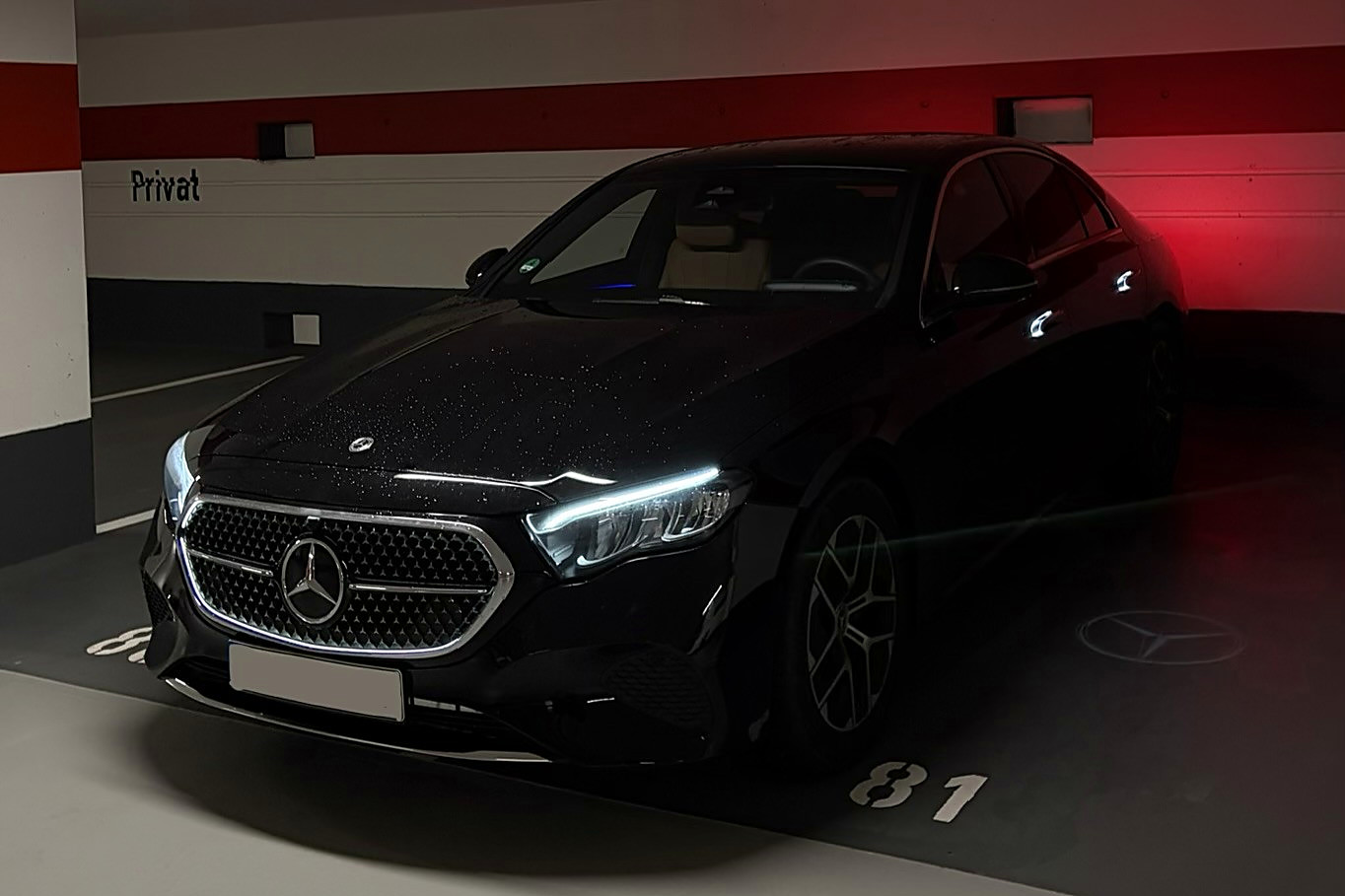 Schwarze Mercedes E-Klasse bei Nacht in einer Tiefgarage — auf den Boden projizierter Stern
